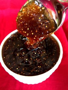 a spoon full of sauce being poured into a white bowl on a red tablecloth