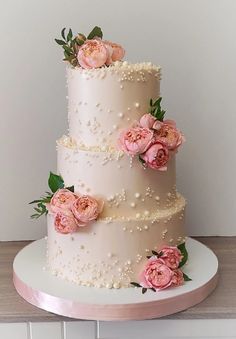 a three tiered wedding cake with pink flowers on top and pearls around the edges