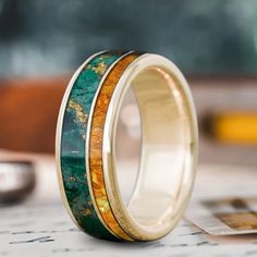 two wedding bands with gold and green wood inlays on top of each other