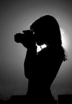 the silhouette of a woman holding a camera up to her face with the sun in the background