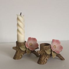 a candle holder with two flowers on it and a white candle in the middle, sitting next to each other