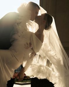 a bride and groom kissing in front of a window with the sun shining on them