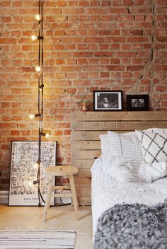 a bedroom with brick walls and lights on the headboard is decorated in neutral colors