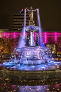 a fountain in front of a building with lights on it and a statue at the top