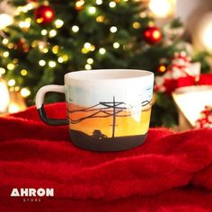 a coffee cup sitting on top of a red blanket next to a christmas tree with lights in the background