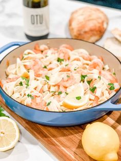 a blue skillet filled with pasta and shrimp next to lemons on a cutting board