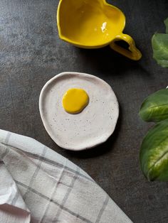 an egg is sitting on a plate next to a cup and saucer with a green leafy plant in the background