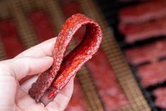 a hand holding up a piece of food on top of a bbq grill covered in ketchup