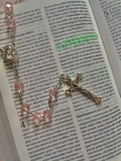 an open book with a cross and rosary on it's side, next to a pair of pink crystal beads