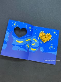 an open book with a heart shaped hole in the middle and blue paper on top