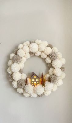 a white wreath with pom - poms hanging on the wall next to a small house