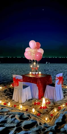 the table is set up on the beach with candles and balloons in the shape of flowers