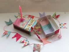 an open box with a candle on it next to some paper flags and bunting