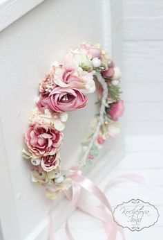 a wreath made out of flowers and ribbons on a white wall with a pink ribbon