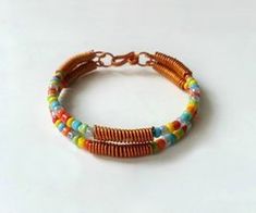 two bracelets with multi colored beads and gold chains on a white surface, one is made from copper wire