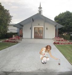 a woman kneeling on the ground in front of a church with a bottle of wine