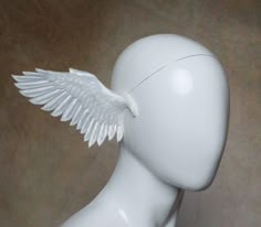 a white mannequin head with an angel wing on it's back side