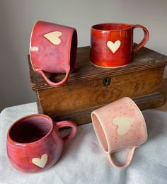 three red mugs with hearts on them are sitting on a table next to a wooden box