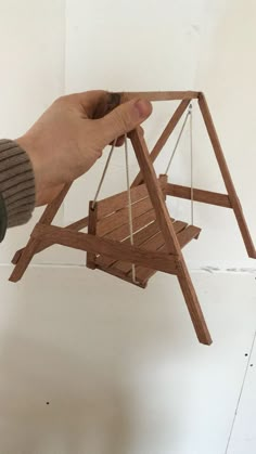 a hand holding a miniature wooden swing with strings attached to the top and bottom, in front of a white wall