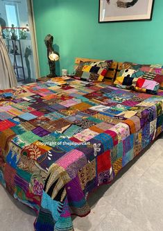 a bed covered in multi colored quilts next to a wall with a painting on it