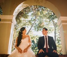 a bride and groom are sitting on the steps in front of an arched doorway looking at each other