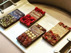 four different types of chocolates sitting on a white tray with red flowers and nuts