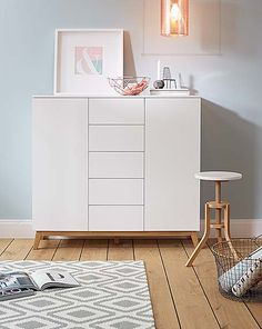 a white dresser sitting on top of a hard wood floor next to a rug and lamp