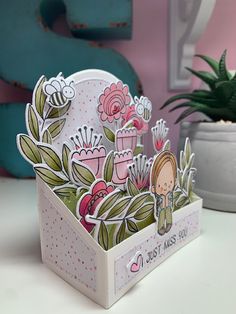 a card in a box with flowers on it and a potted plant next to it