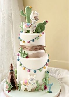 a three tiered cake decorated with llamas, cactuses and other decorations