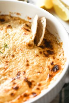 a close up of a bowl of food with a spoon in it and lemon wedges on the side