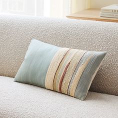 a white couch with a striped pillow on it's back and a wooden table in the background