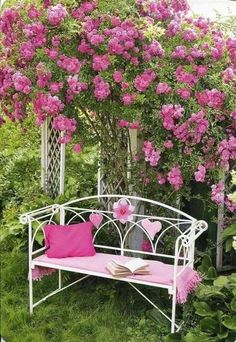 a white metal bench with pink cushions under a blooming tree and shrubbery in the background