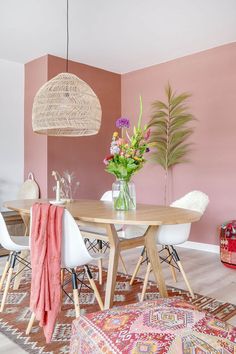 a dining room with pink walls and rugs on the floor, white chairs and a round wooden table