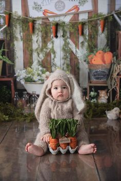 a baby is sitting on the floor with carrots in their hands and wearing a bunny costume