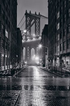 a black and white photo of a city street at night with the brooklyn bridge in the background