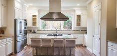 a kitchen with white cabinets and an island in the middle is surrounded by bar stools