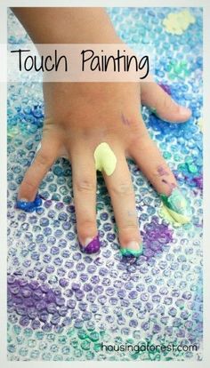 a child's hand with green, purple and blue nail polish sitting on top of a table