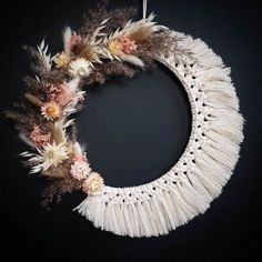 a white wreath with feathers and flowers hanging on a black wall in front of a dark background