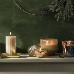 three candles are sitting on a mantle with pine branches in the back ground and green wall behind them