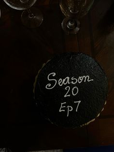 a black cake sitting on top of a wooden table next to wine glasses and candles