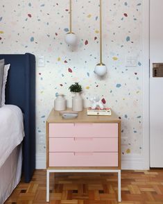 a bedroom with a pink dresser next to a white bed and wallpapered walls