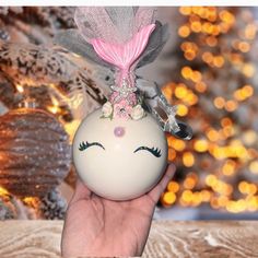 a hand holding a white ornament with a pink flower on it's head