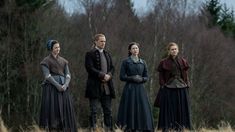 four people standing in a field with trees behind them