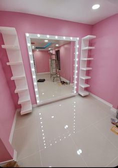 a pink room with white shelves and lights on the walls, and a large mirror in the middle