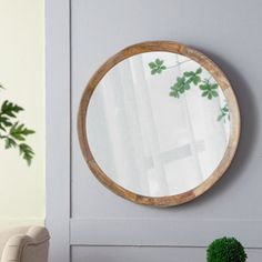 a round wooden mirror hanging on the wall above a small table with potted plants