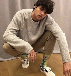 a young man sitting on the floor with his hands in his pockets and wearing sneakers