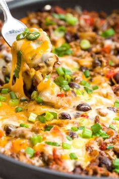 a spatula scooping some food out of a skillet filled with beans, cheese and other toppings