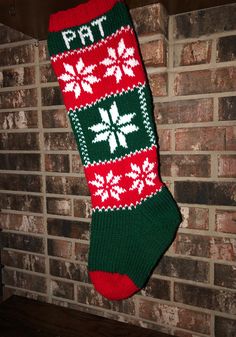 a green and red knitted christmas stocking hanging on a brick wall next to a fireplace