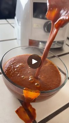 a person pouring sauce into a glass bowl on top of a counter with food in it