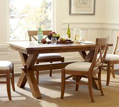 a dining table with four chairs and a bench in front of it, next to a window